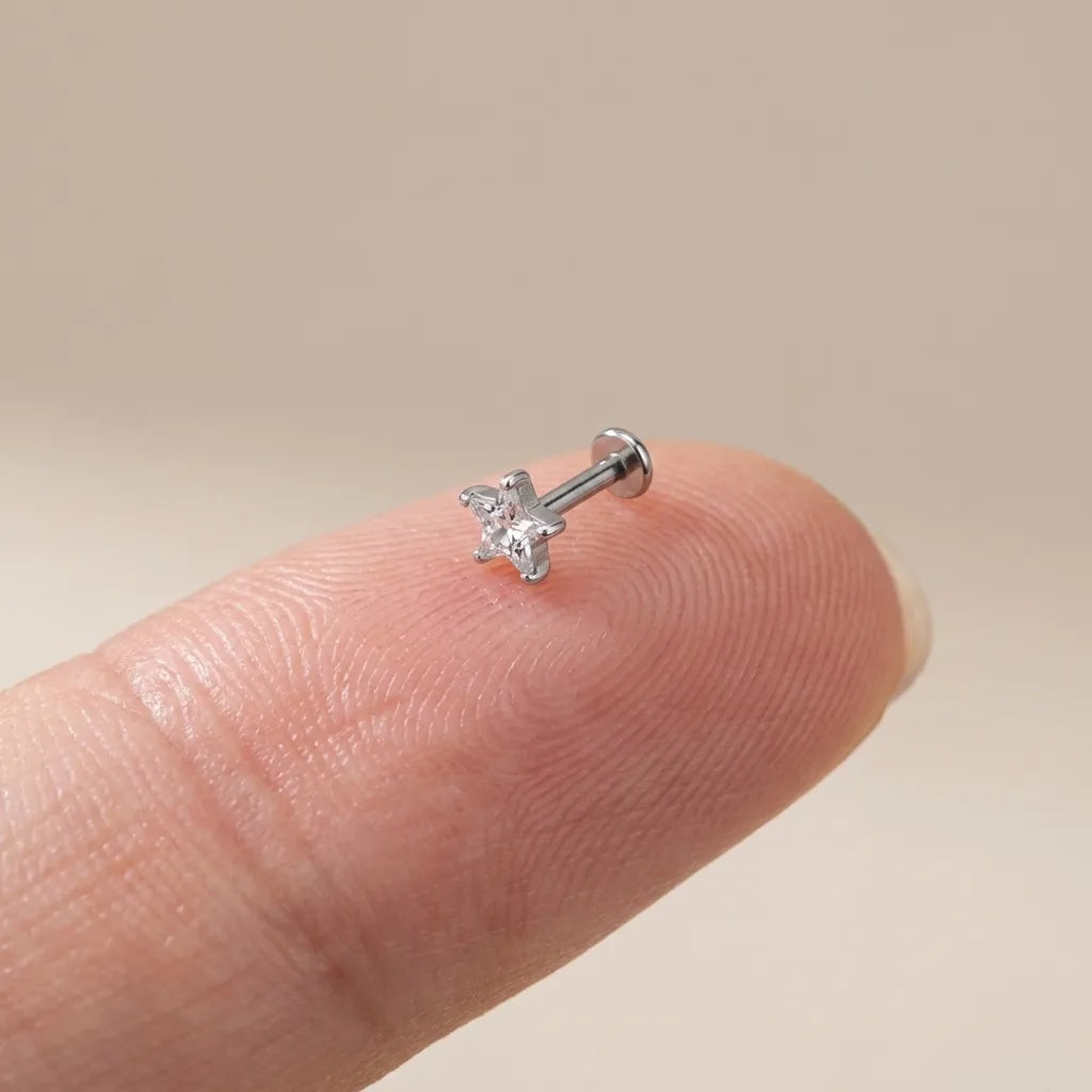 Flat back titanium Ashley star cut labret shown on a fingertip for scale
